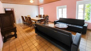 A room with a wooden ceiling, tiled floor, a dining table with chairs, a sofa, and a cabinet.