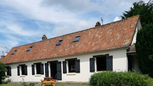 A white building with a red-tiled roof, multiple windows with shutters, and a gravel driveway.