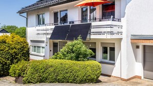 Ein zweistöckiges Wohngebäude mit Balkon, Solaranlage und einem roten Sonnenschirm.