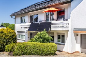 Un edifici residencial de dos pisos amb un balcó, panells solars i un para-sol vermell.