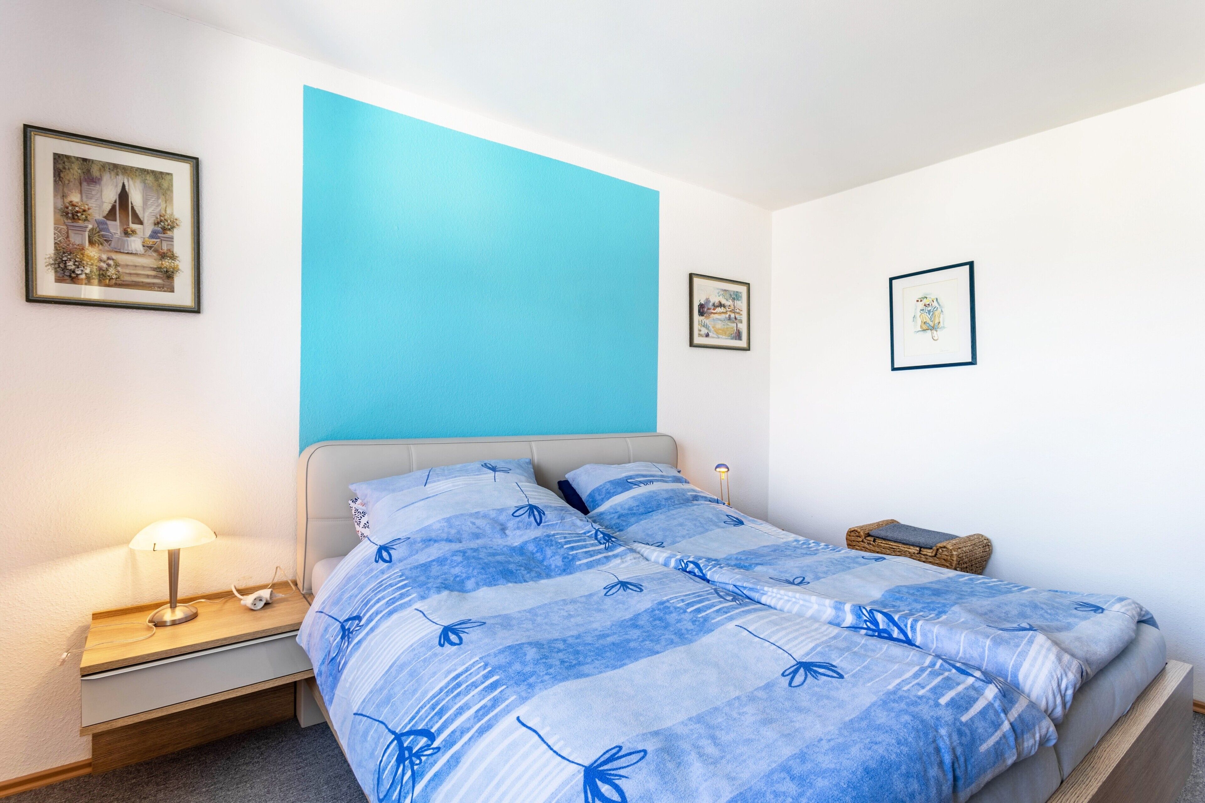 A bedroom with a bed, nightstand, lamp, and wall art.