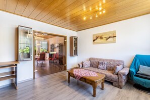 A living room with a wooden ceiling, a sofa, a coffee table, and a glass door leading to a dining area. - Gierske Apartment with Mountain View and Shared Garden (Olsberg)