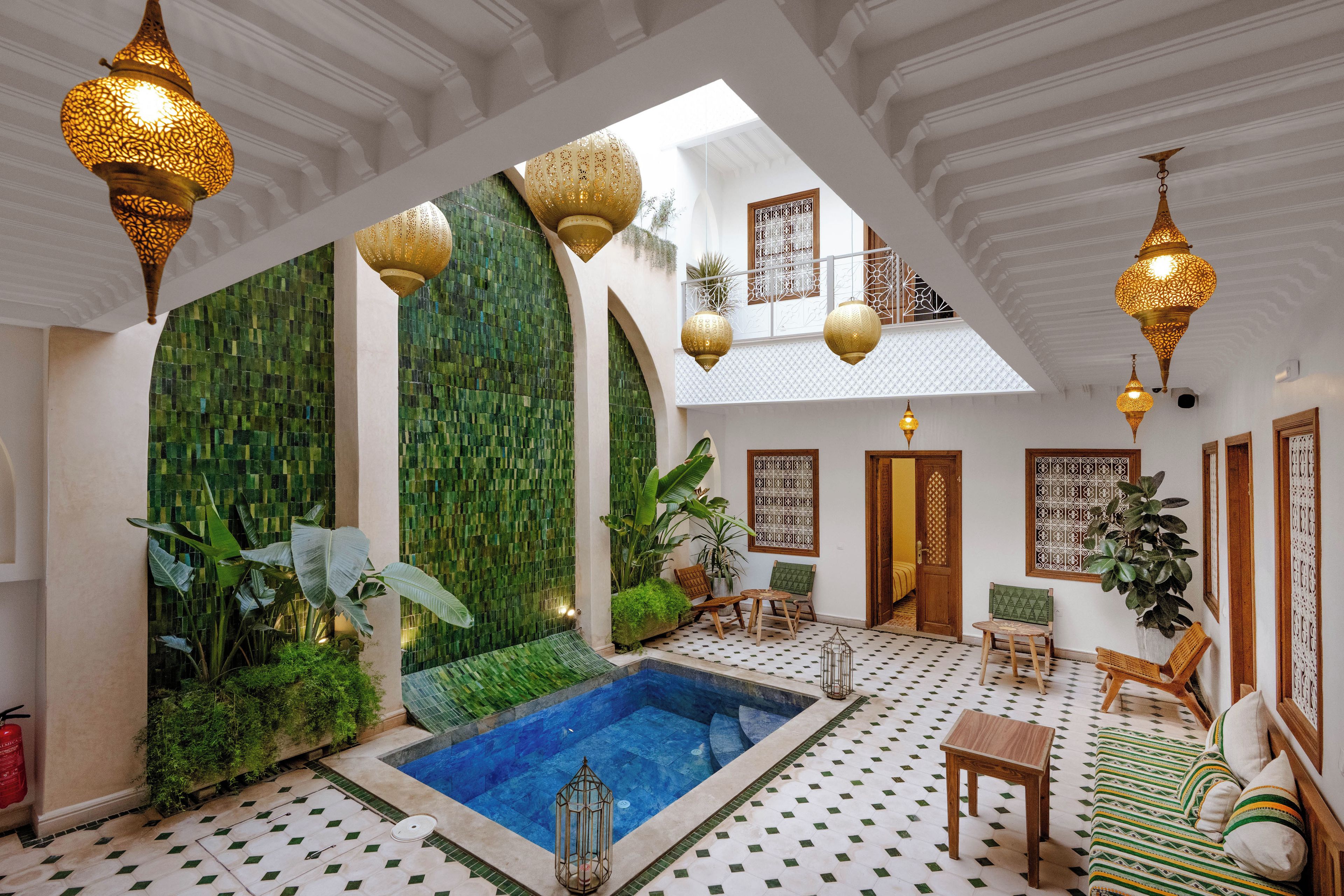 Habitación de hotel con piscina, paredes de mosaicos verdes y decoración tradicional.