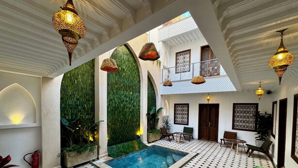 A luxurious indoor pool area with a geometric tiled floor, a central pool, and ornate hanging lamps. - Riad Jo (Marrakech)