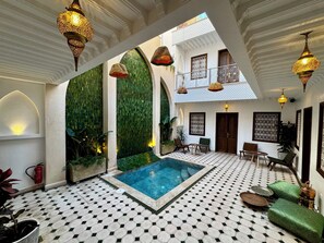 A luxurious indoor pool area with a geometric tiled floor, a central pool, and ornate hanging lamps. - Riad Jo (Marrakech)