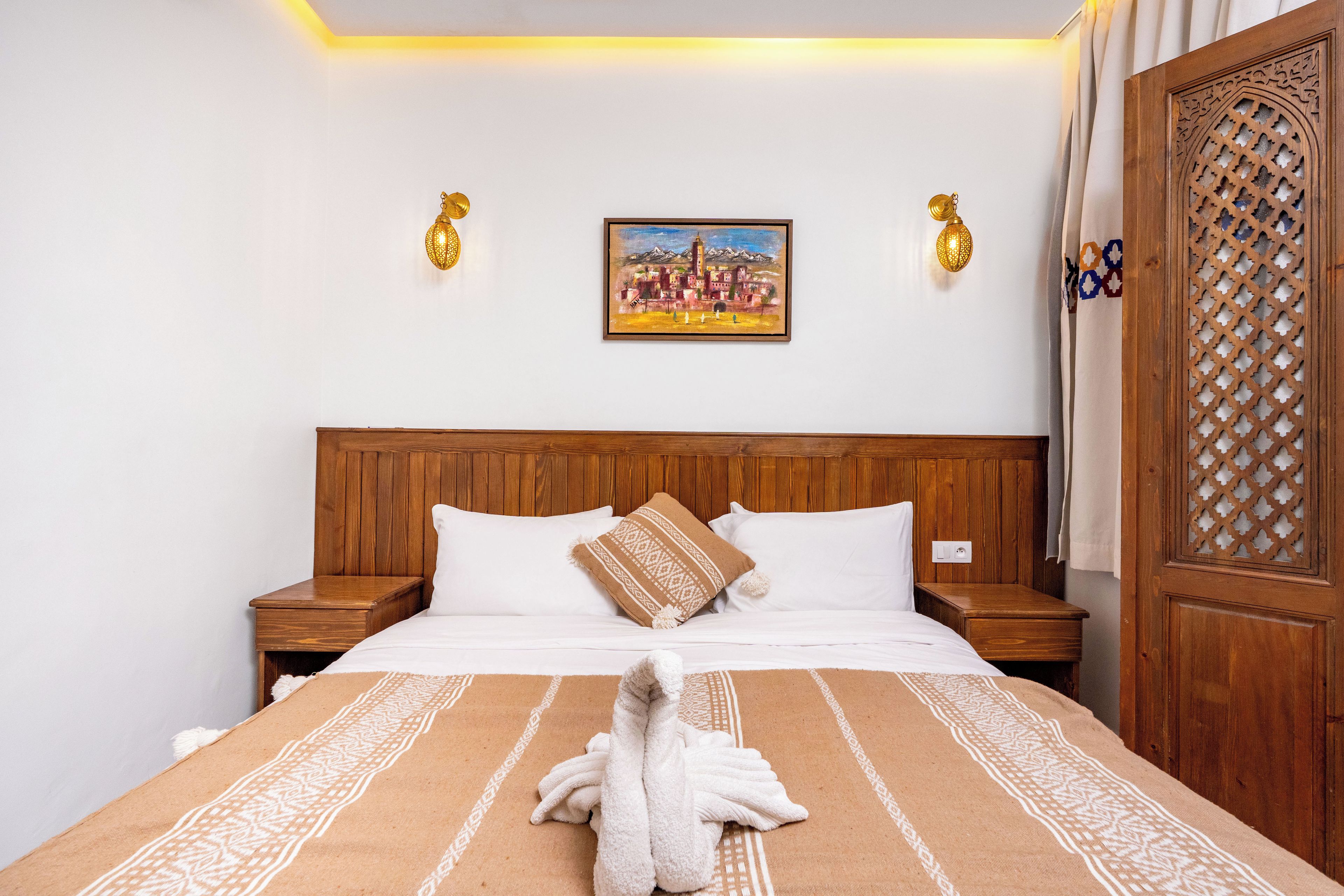 Ein Hotelzimmer mit einem hölzernen Kopfteil, einem Gemälde über dem Bett und einem Vorhang mit traditionellem Muster.