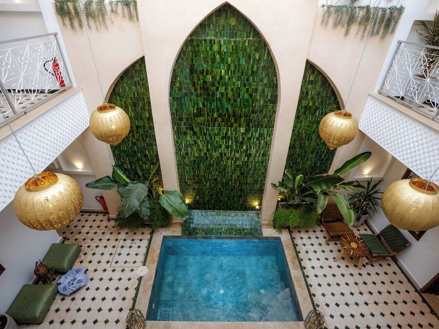Un área de piscina con una piscina rectangular central, rodeada de suelo estampado y flanqueada por paredes de mosaico verde y faroles colgantes.