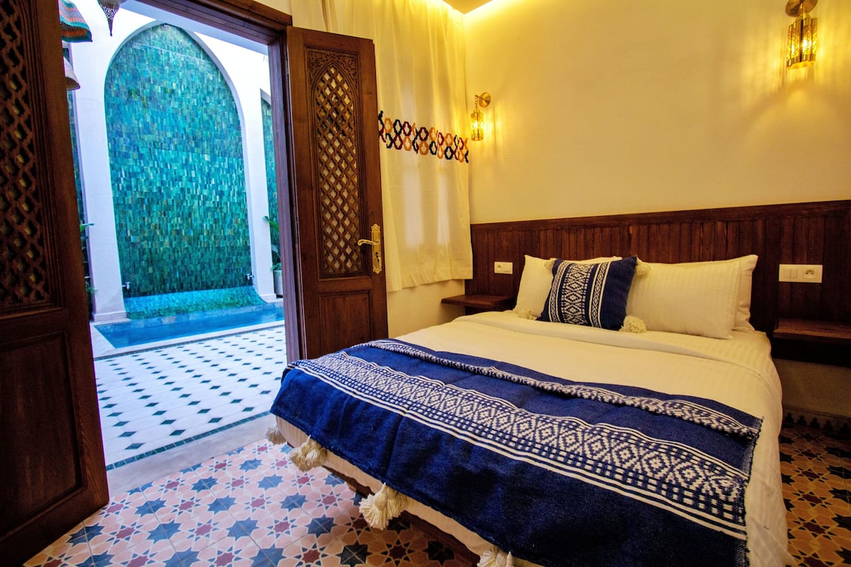 A bedroom with a large bed, a patterned rug, and a view of a courtyard through an open door.
