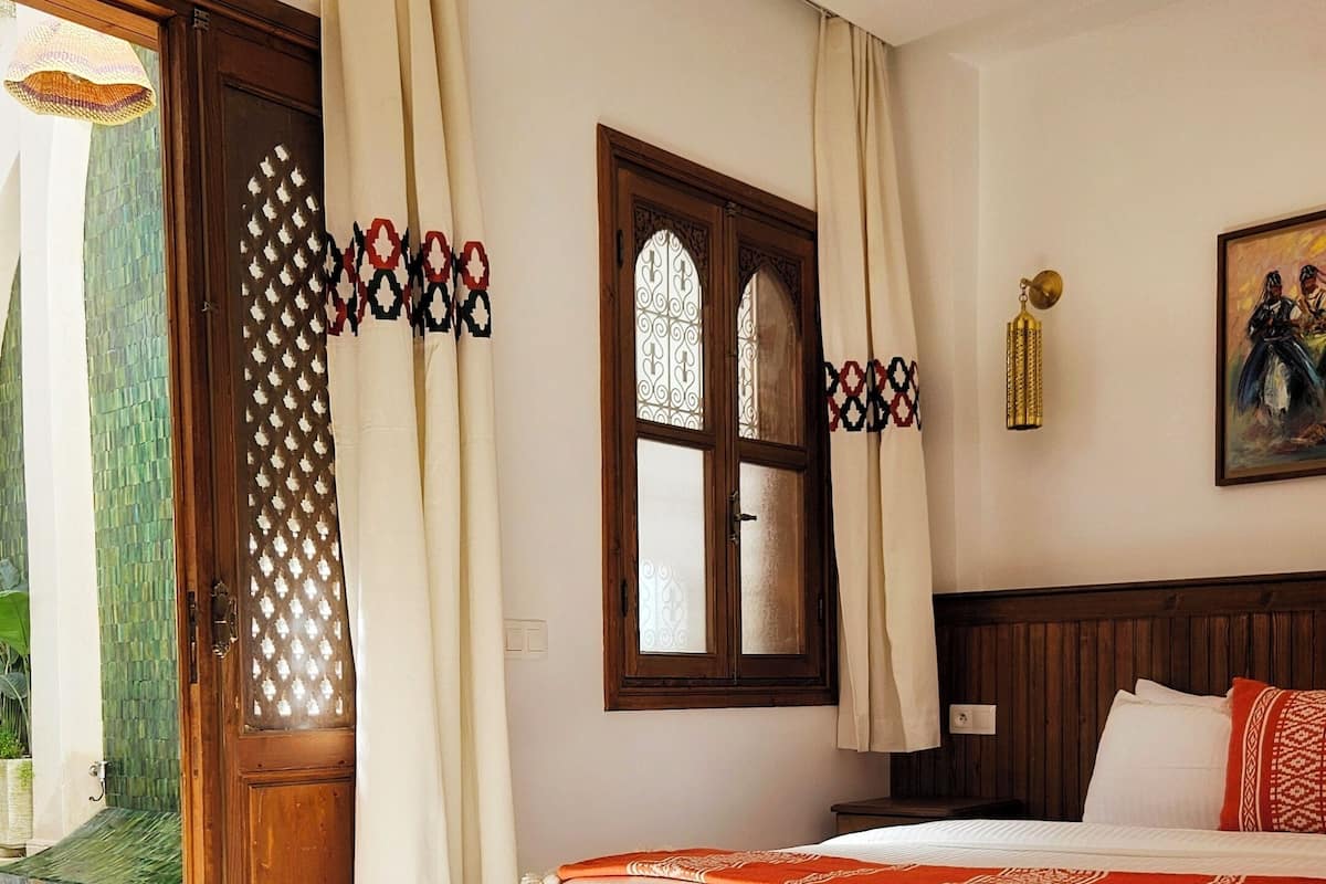A bedroom with a bed, a window, a door, and a small table.