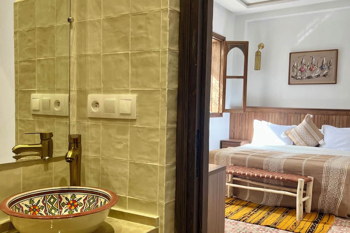 A bathroom with a beige tiled wall, a sink with a decorative bowl, a towel rack, and a mirror.
