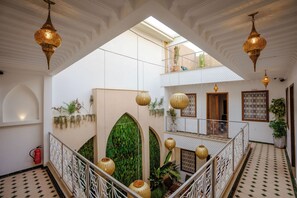 Ein mehrstöckiger Innenraum mit aufwendigen Leuchten, einer grünen Mosaikwand und einem Balkon mit Pflanzen.