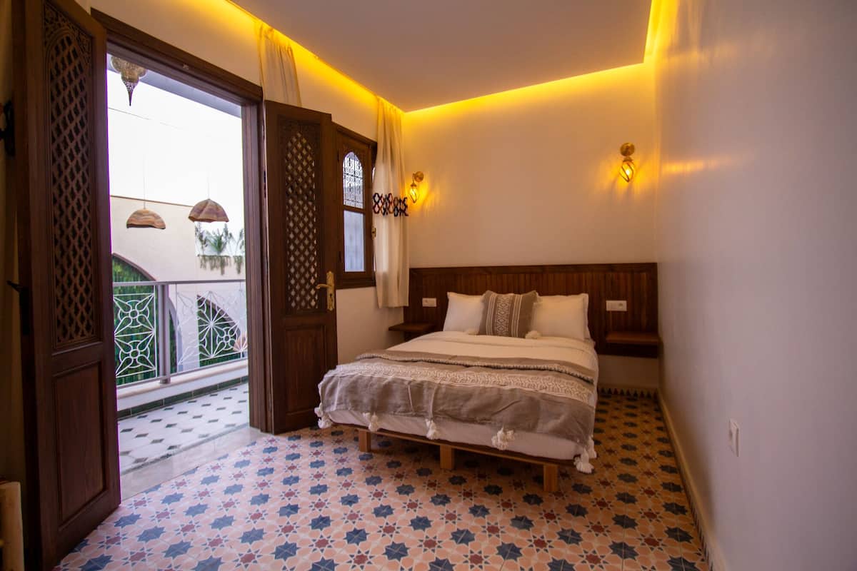A bedroom with a bed, patterned floor, and a balcony with a railing.