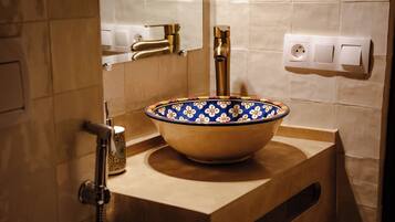 Un baño con encimera color beige, un lavamanos tipo cuenco con estampado azul y blanco, grifo dorado y ducha de mano.