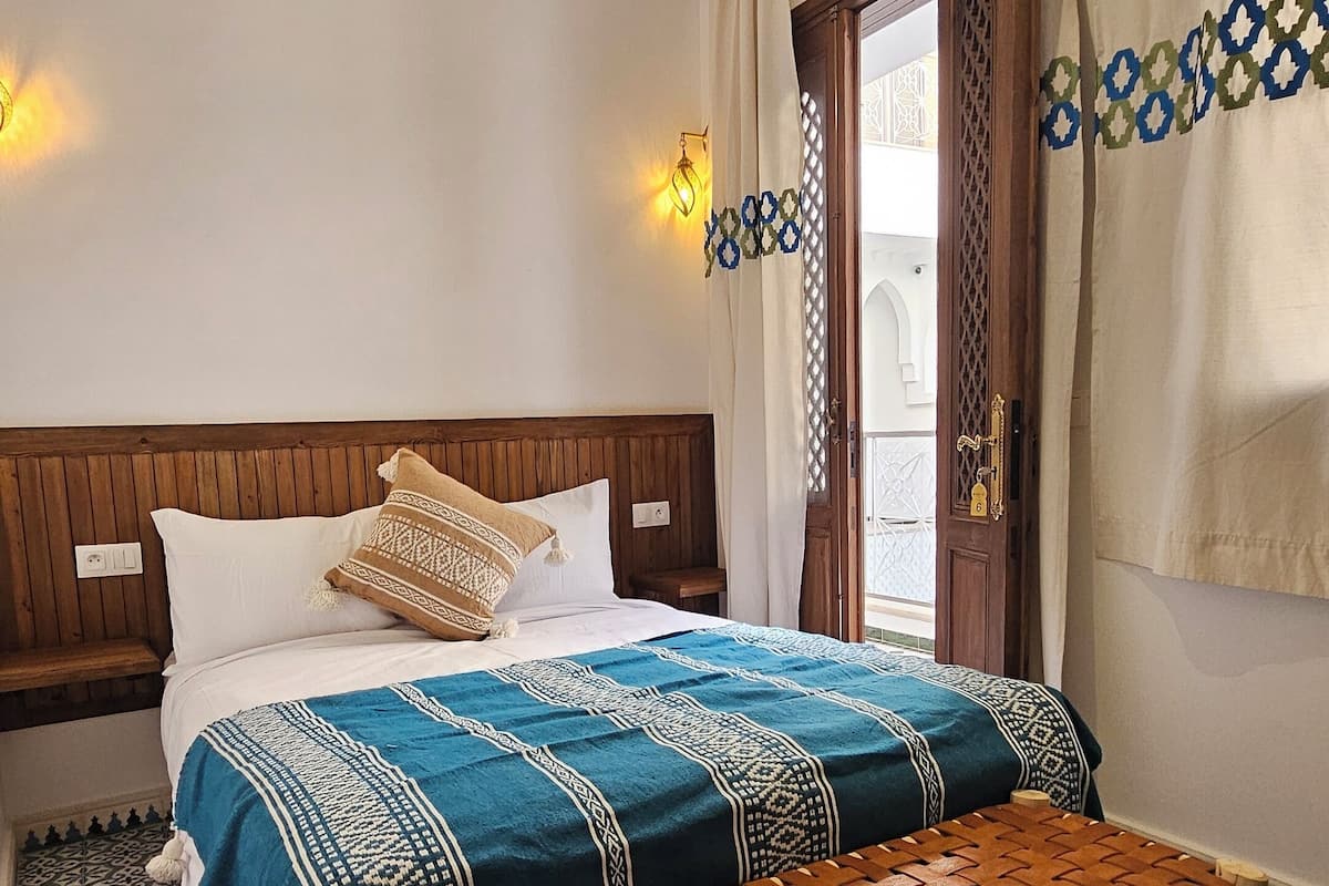 A bedroom with a wooden headboard, a bed with patterned bedding, a bench, and patterned floor tiles.