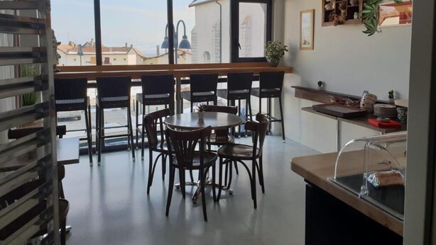 A modern dining area with a large window, a wooden table, and several chairs. - Auberge Communale - La Fruitière Péron (Péron)