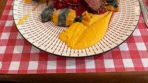 A plate of food with a slice of meat and yellow fruit on a checkered tablecloth. - Auberge Communale - La Fruitière Péron (Péron)