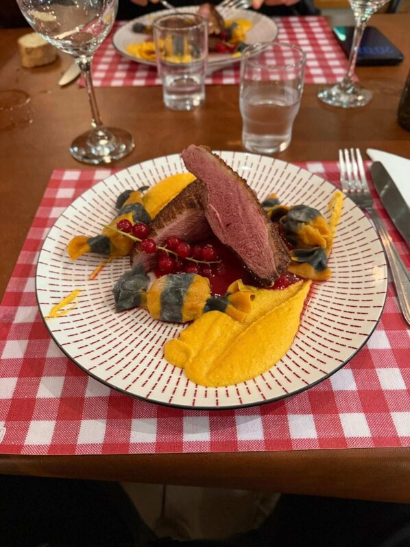 A plate of food with a slice of meat and yellow fruit on a checkered tablecloth. - Auberge Communale - La Fruitière Péron (Péron)
