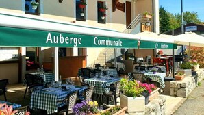 An outdoor dining area with tables and chairs, a green awning with the text "Auberge Communale," and a staircase leading to an upper level. - Auberge Communale - La Fruitière Péron (Péron)