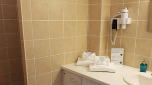 A bathroom with beige tiles, a white toilet, a sink, and a hairdryer on the wall. - Auberge Communale - La Fruitière Péron (Péron)