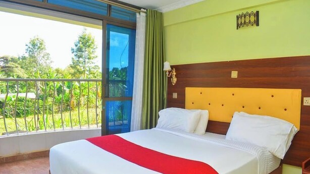 A hotel room with a large bed, a wooden headboard, a balcony with a view of greenery, and a window with curtains. - Aberdare gardens and resort karatina (Karatina)