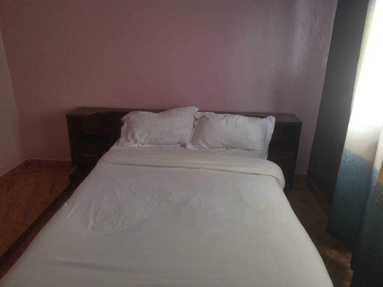 En säng med vita sängkläder i ett rum med rosa väggar och ett trägolv.