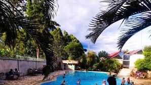 A swimming pool surrounded by hexagonal tiles, with people swimming and lounging. - Aberdare gardens and resort karatina (Karatina)