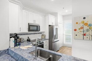 A modern kitchen with white cabinets, stainless steel appliances, a marble countertop, and a sink. - Chic coastal living meets resort-style amenities! (Longboat Key)