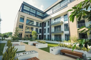 Een modern gebouw met meerdere verdiepingen, grote ramen en een aangelegde binnentuin met bankjes en plantenbakken.
