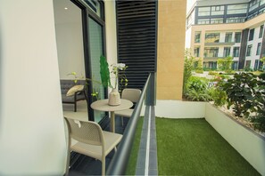 Een klein balkon met een tafel, stoelen, een plant in pot en uitzicht op een gebouw met balkons.