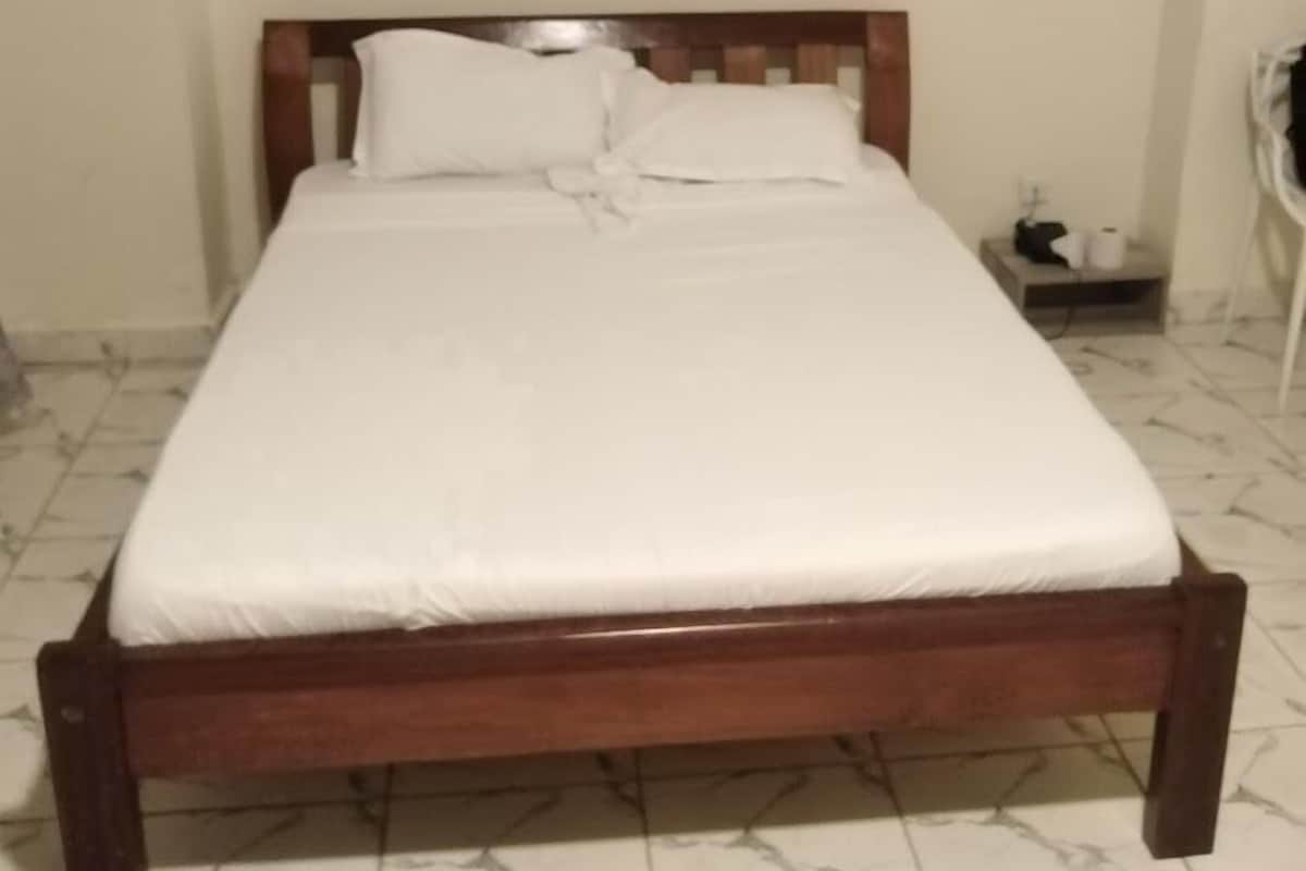 A single bed with a wooden frame and white bedding in a room with white walls and tiled flooring.