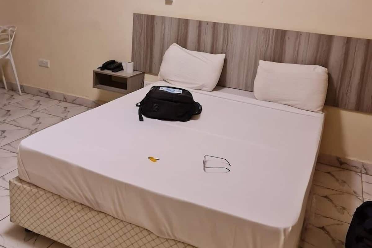 A hotel room with a bed, a nightstand, a chair, and a wall-mounted air conditioner.