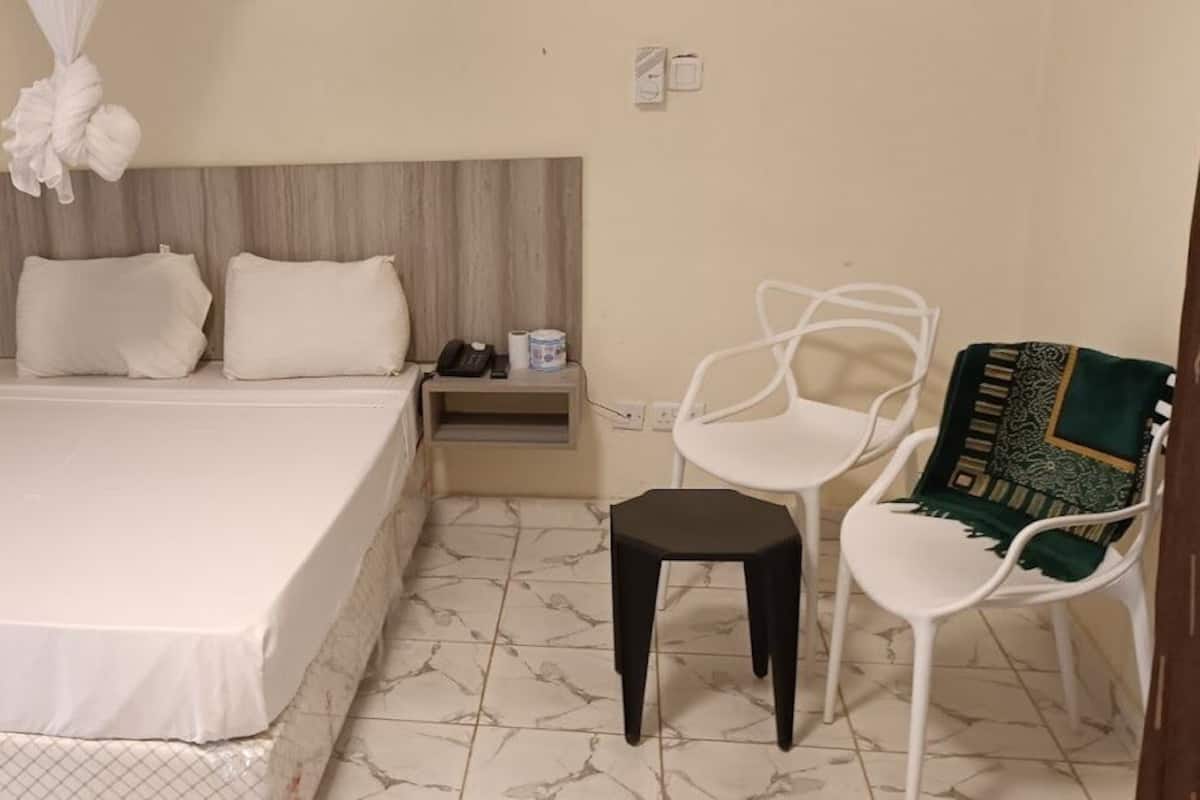 A hotel room with a large bed, a nightstand, a chair, and a small stool.