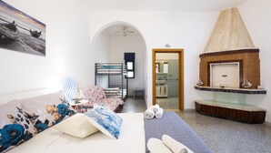 Habitación de hotel con litera, sofá tapizado con motivos florales, chimenea y vista al mar a través de un arco.