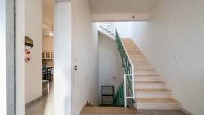 Una escalera con barandilla verde que conduce a una plataforma, suelo de baldosas y una puerta que da a una habitación con zona de cocina visible.