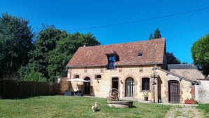Une maison de campagne en pierre, avec un toit en pente, un petit balcon et une grande roue dans la cour.