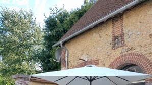 Une terrasse extérieure avec un parasol blanc, des meubles en osier noir et un bâtiment en briques en arrière-plan.