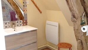 Une salle de bain avec une poutre en bois, un lavabo avec un miroir, des toilettes et un petit tabouret.