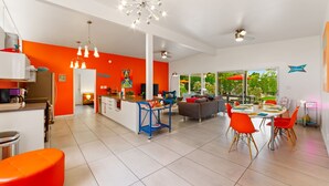 A modern kitchen with a central island, bright orange walls, and a dining area with orange chairs. - 30+ Stay! Perfect For Families, W/Pool & Hot Tub (Palm Springs)