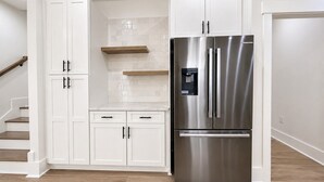 Eine moderne Küche mit weißen Schränken, einem Edelstahlkühlschrank und einer Holztreppe.