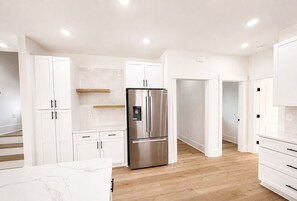 A modern kitchen with white cabinetry, a stainless steel refrigerator, and wooden flooring. - 5 Bedroom, Private Pool, Elevator - New Construction - Why Knot (Surfside Beach)