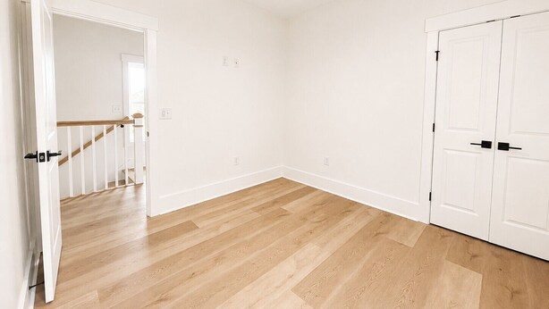Ein Zimmer mit Holzboden, weißen Wänden, Deckenventilator und einer Tür mit schwarzem Griff.