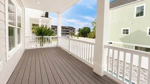 Eine überdachte Veranda mit Holzterrasse, weißen Geländern und Blick auf die Nachbargebäude.