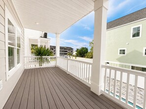 A covered porch with a wooden deck, white railings, and a view of neighboring buildings. - 5 Bedroom, Private Pool, Elevator - New Construction - Why Knot (Surfside Beach)