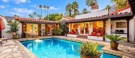 A pool area with a stone deck, lounge chairs, and a covered seating area with red cushions.