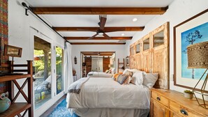 Ein Schlafzimmer mit einem großen Bett, Holzbalken, einem Deckenventilator und Blick ins Freie.