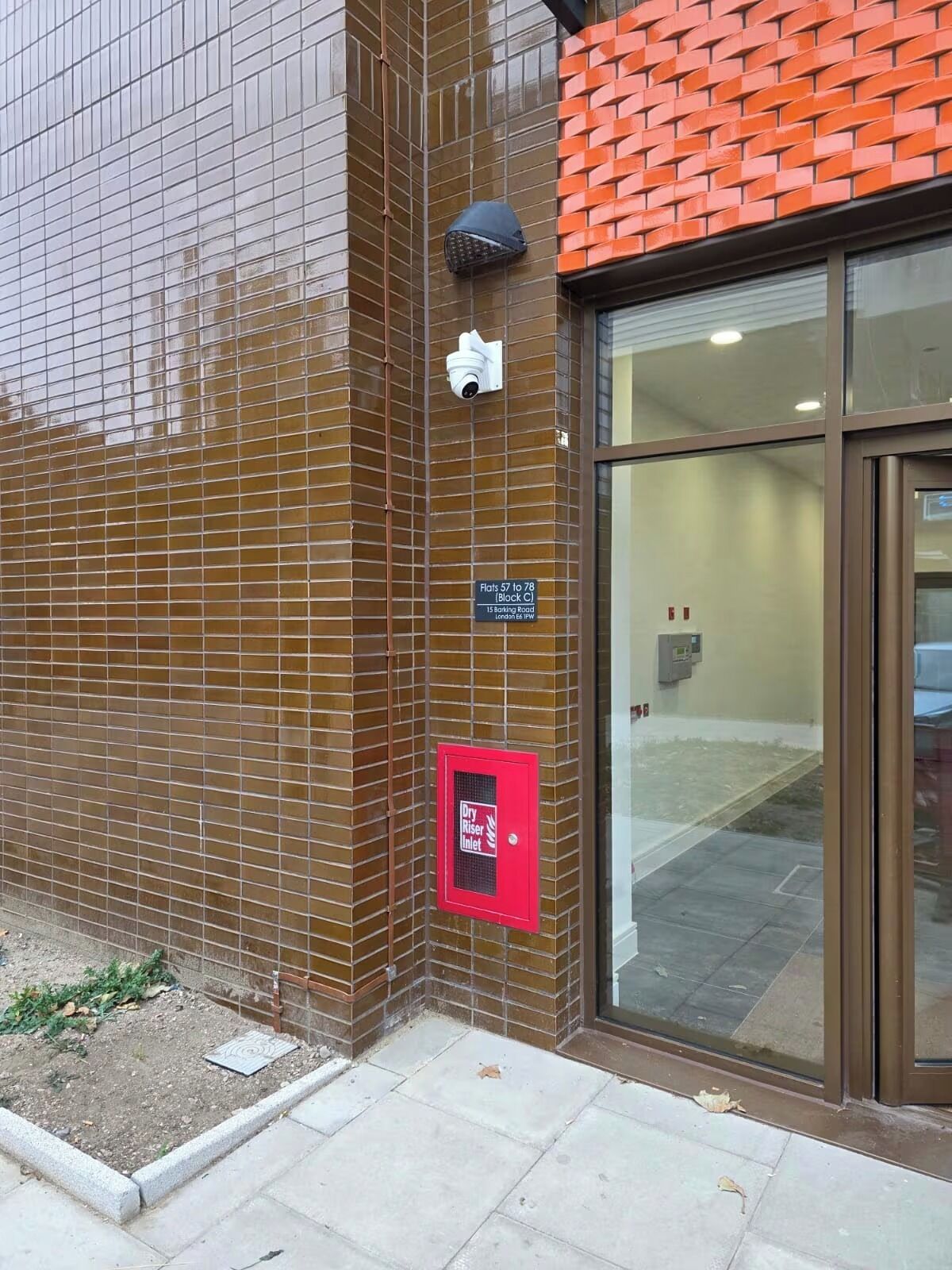 A building with a tiled facade, a security camera, a fire alarm, and a sign indicating flats 57 to 78.