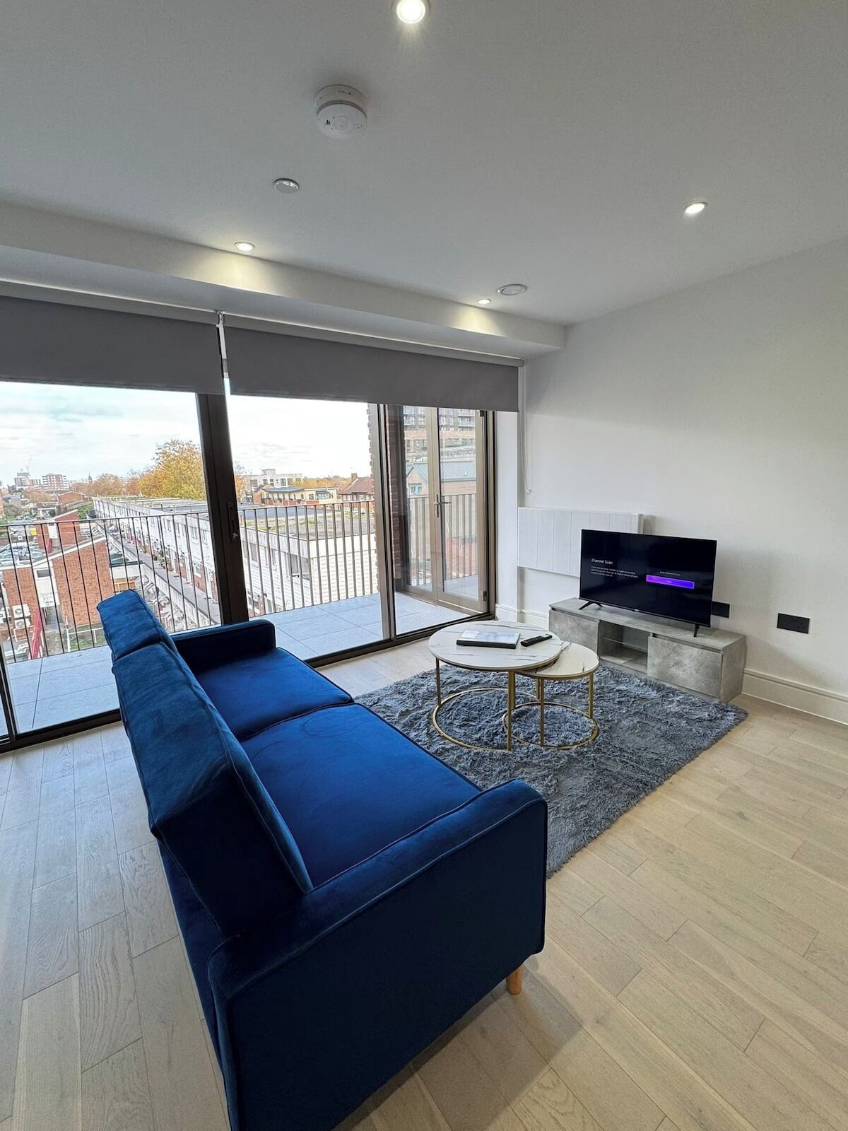 A modern living room with a blue sofa, a small round table, and a TV on a stand.