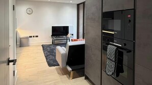 Eine moderne Küche mit Einbauofen und Mikrowelle, ein Essbereich mit Tisch und Stühlen sowie ein Wohnzimmer mit Sofa und Fernseher.