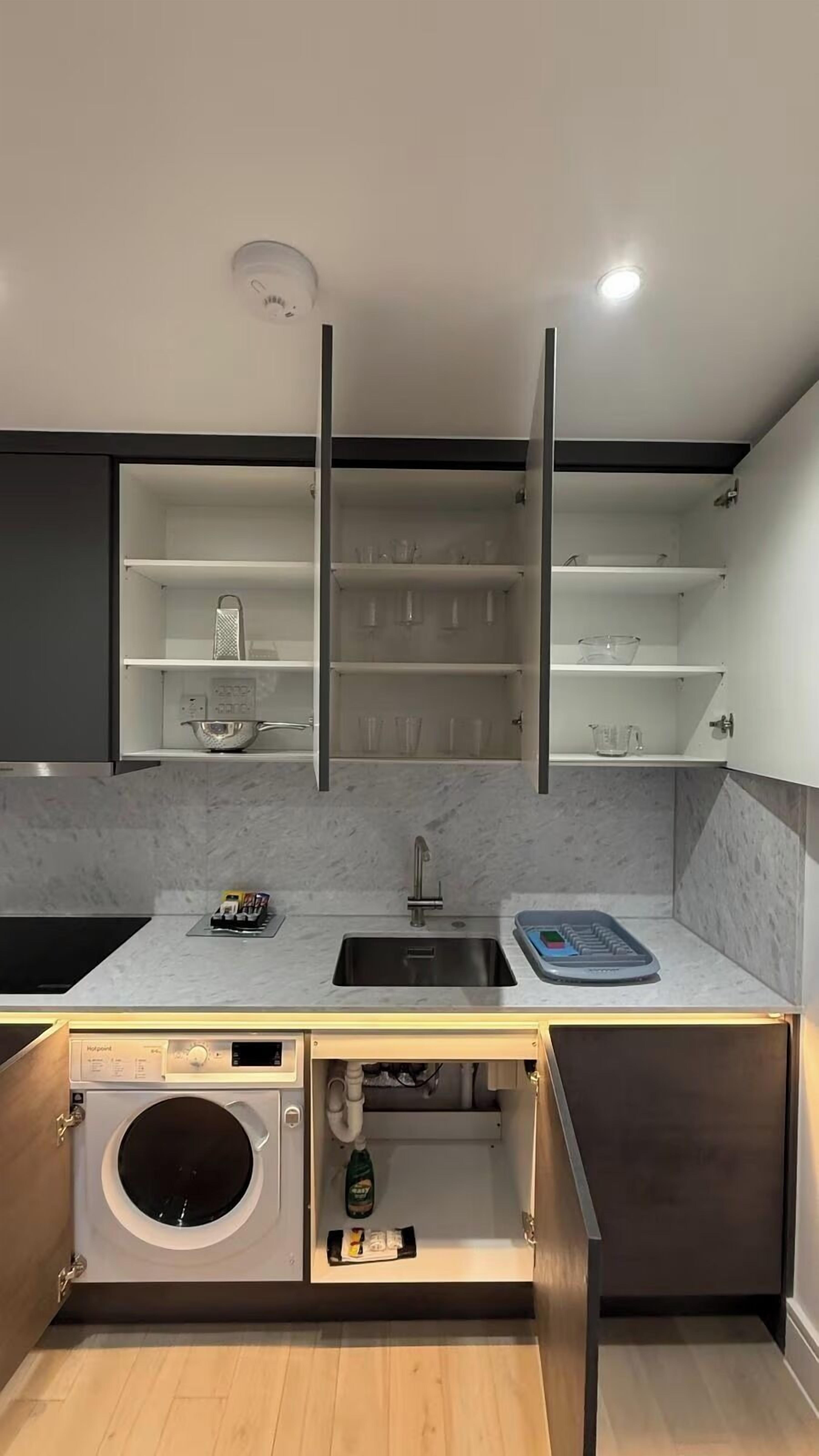 A compact kitchen with a built-in washing machine, a sink, and open shelving above.