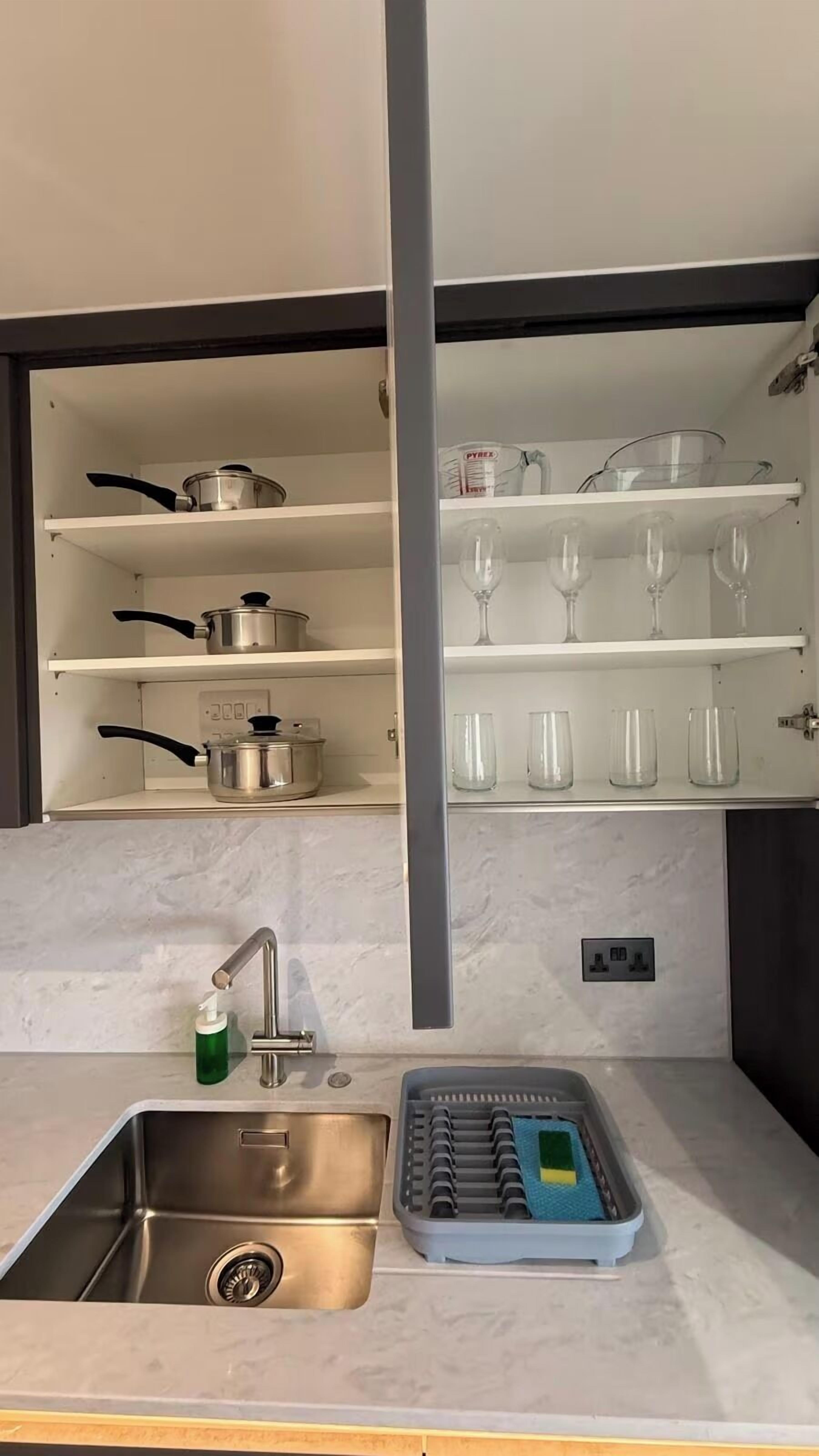 A kitchen with a built-in sink, stainless steel cookware, and glassware on shelves.